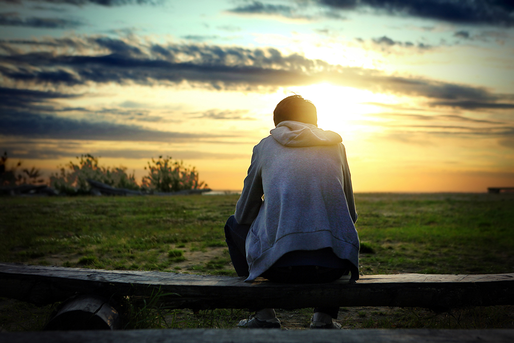 Lonely Person sits on the Bench at Sunset Background