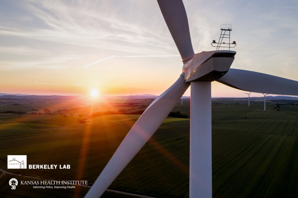 A close-up aerial view of a large wind turbine set against a green rural landscape, with the sun setting on the horizon and casting a warm orange glow over the fields, featuring logos for Berkeley Lab and Kansas Health Institute in the lower left corner.