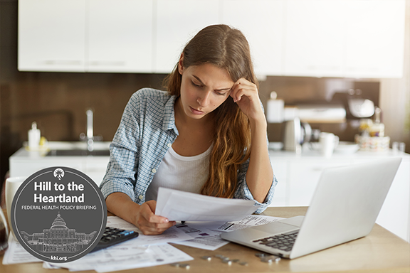 A young woman sits in front of her computer with a calculator looking puzzled